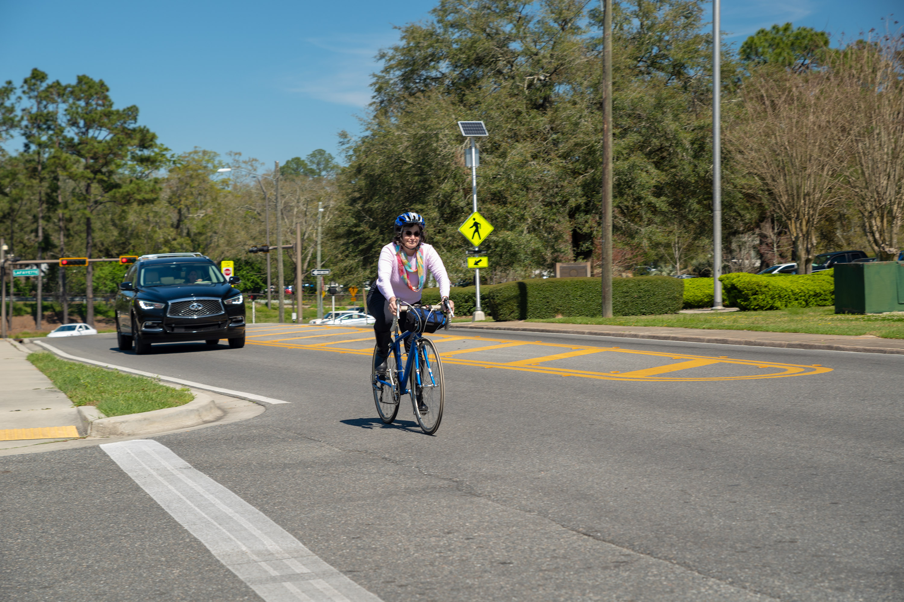 A photo of a Florida roadway where a woman is riding a bicycle and there is a car behind her traveling at a safe distance.